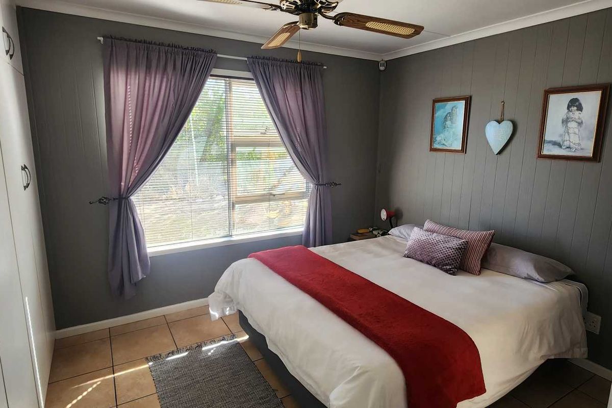 A bedroom featuring built-in cupboards, tiled flooring, and a ceiling fan, with a feature wall finished in grey paneling.