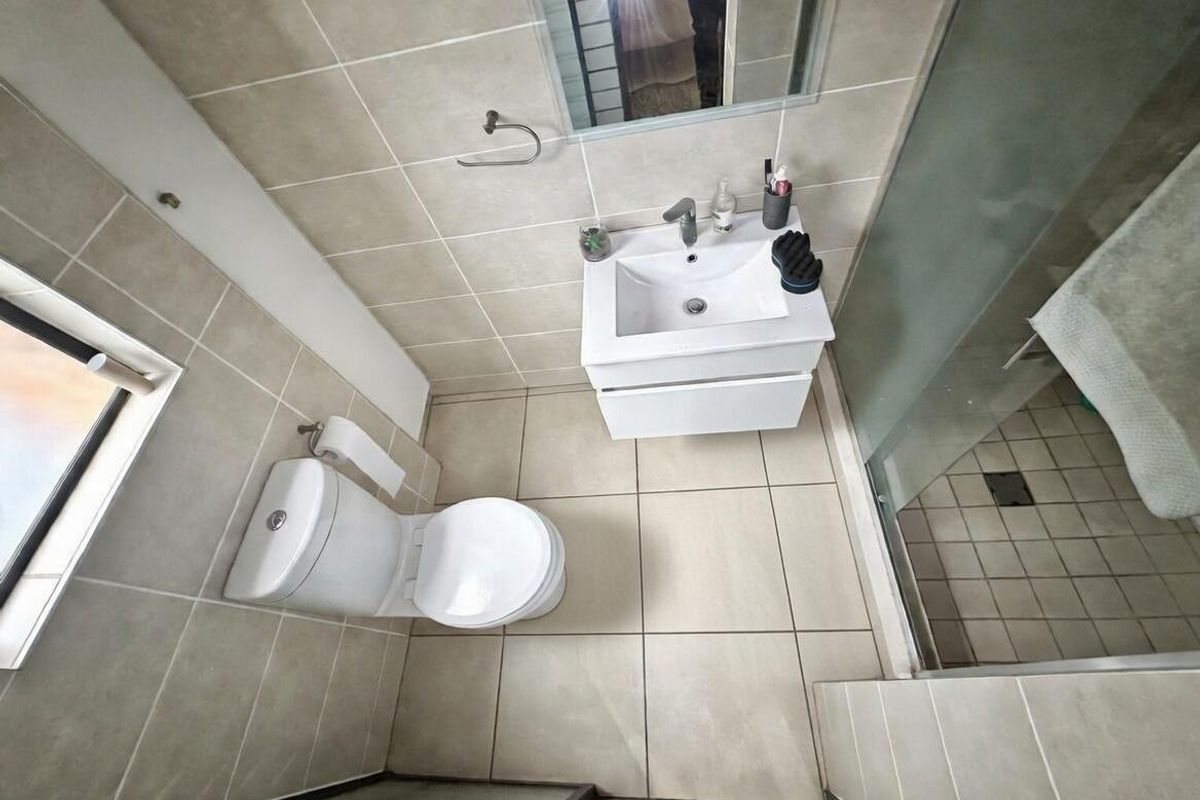 A compact, modern bathroom featuring a wall-mounted vanity with basin, a toilet, and a glass-enclosed shower, finished with neutral floor and wall tiling.