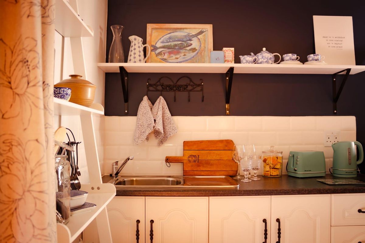 A compact kitchen area featuring white cabinetry, a stainless steel sink with a subway tile backsplash, and dark accent wall shelving.
