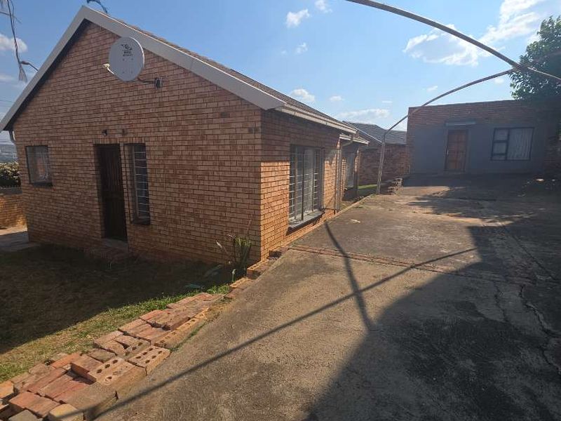 Rear view of a face brick house featuring a concrete driveway, security bars on windows, and a separate outbuilding structure.