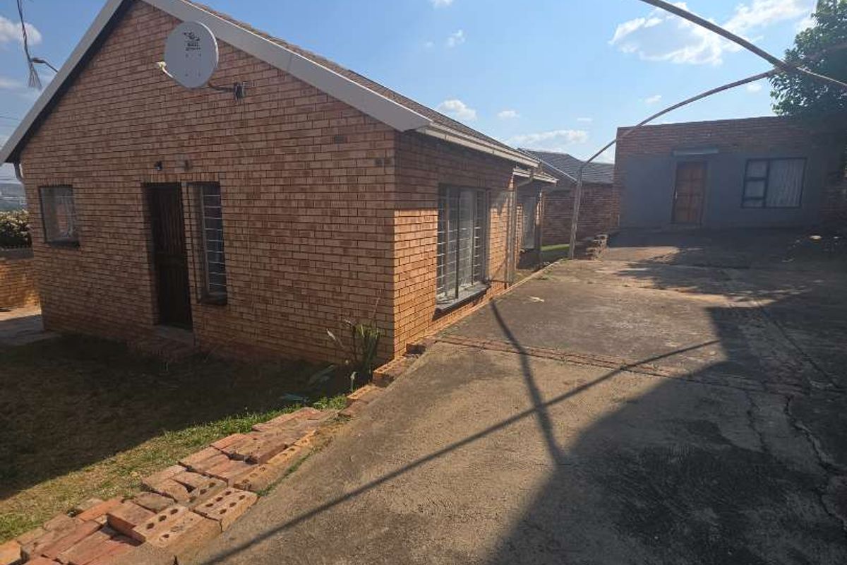 Rear view of a face brick house featuring a concrete driveway, security bars on windows, and a separate outbuilding structure.