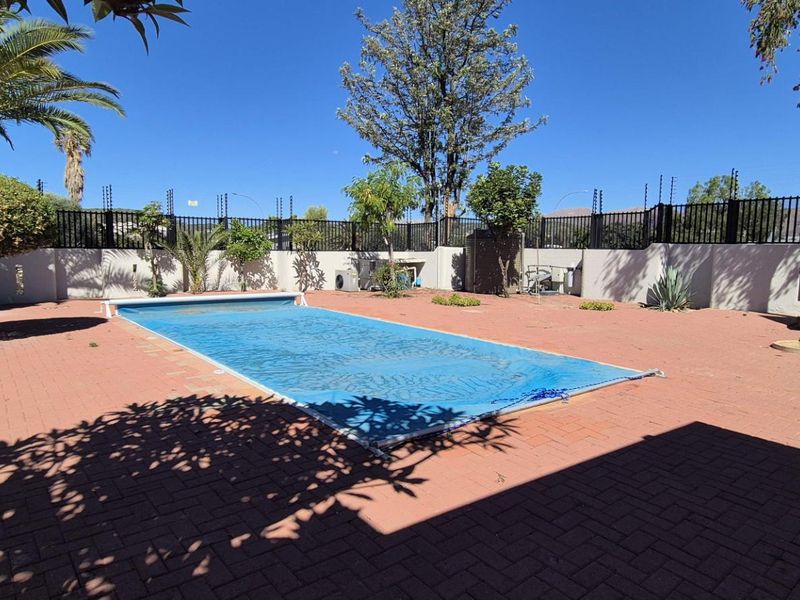 Outdoor pool area featuring a rectangular swimming pool with a cover, surrounded by paved patio space and secure perimeter walling with electric fencing.