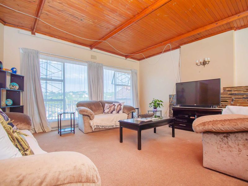 Spacious living room featuring a high exposed timber ceiling, stone fireplace detail, and large windows providing natural light.