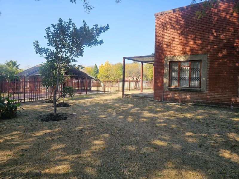 Rear view of the property featuring a brick facade, covered patio area, and a spacious garden enclosed by metal fencing.