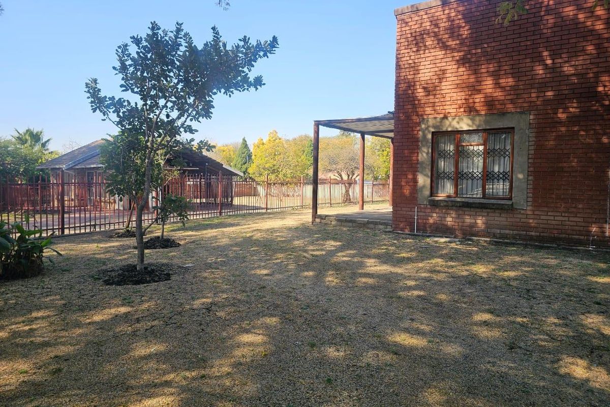 Rear view of the property featuring a brick facade, covered patio area, and a spacious garden enclosed by metal fencing.