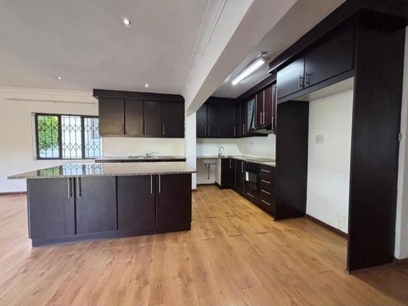 Spacious kitchen featuring dark wood cabinetry, granite countertops, built-in oven, and laminate flooring, offering a functional layout in an open-plan setting.