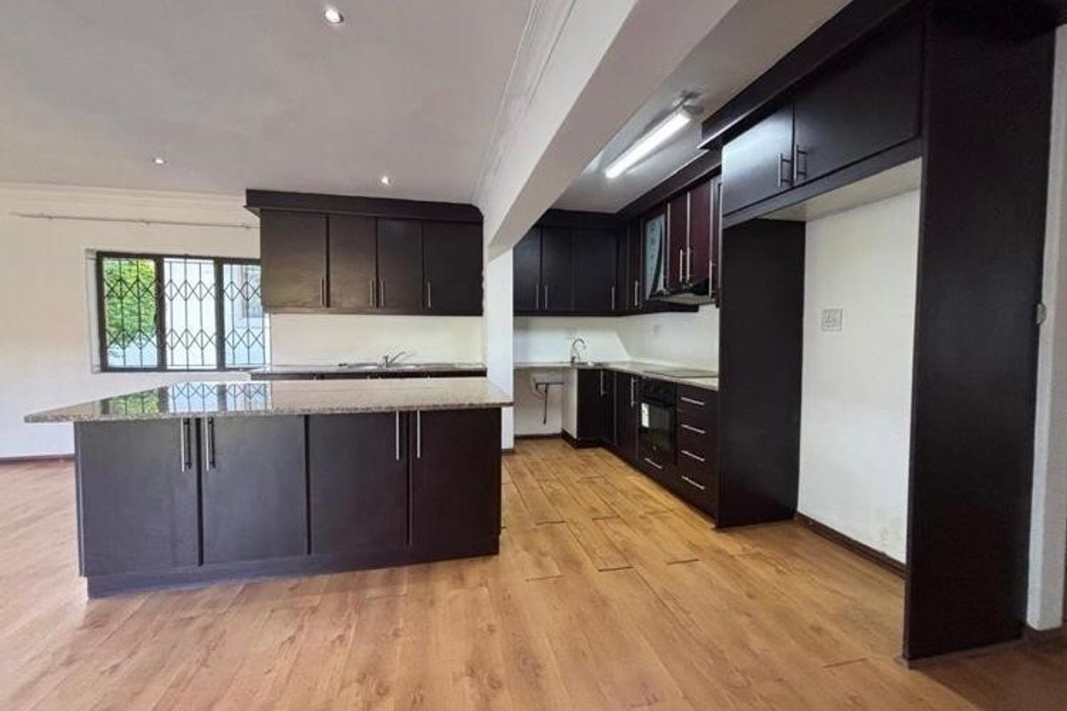 Spacious kitchen featuring dark wood cabinetry, granite countertops, built-in oven, and laminate flooring, offering a functional layout in an open-plan setting.