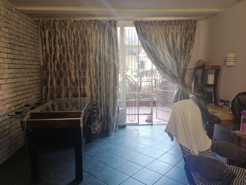 A living area featuring exposed brickwork, tiled flooring, and a security gate leading to an outdoor patio space.