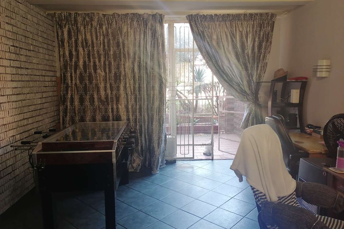 A living area featuring exposed brickwork, tiled flooring, and a security gate leading to an outdoor patio space.