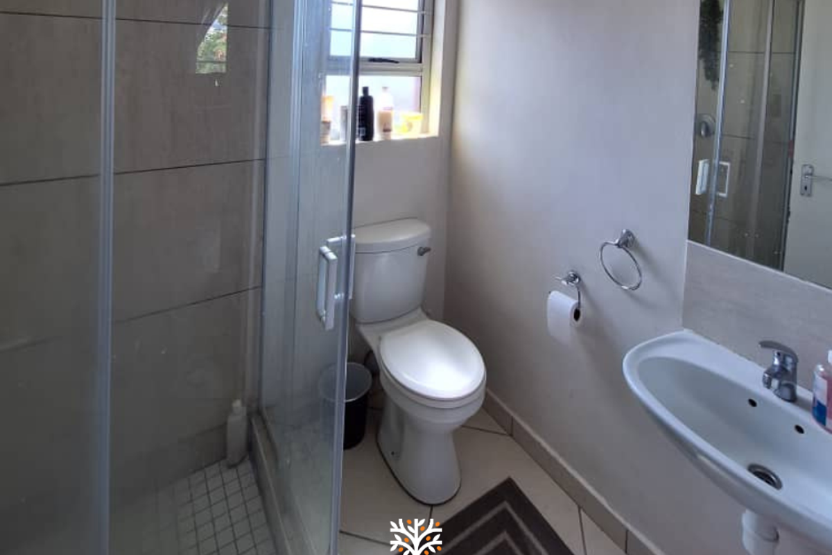 A functional bathroom featuring a glass-enclosed shower, a standard toilet, and a wall-mounted basin with a mirror.