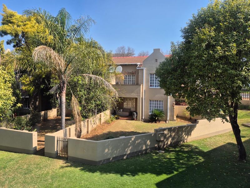 A view of the rear elevation of the apartment building, featuring a private garden area enclosed by a perimeter wall and mature landscaping.