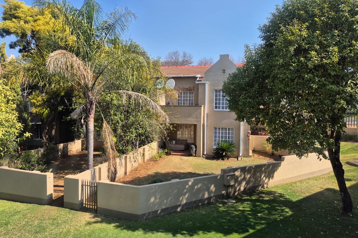 A view of the rear elevation of the apartment building, featuring a private garden area enclosed by a perimeter wall and mature landscaping.