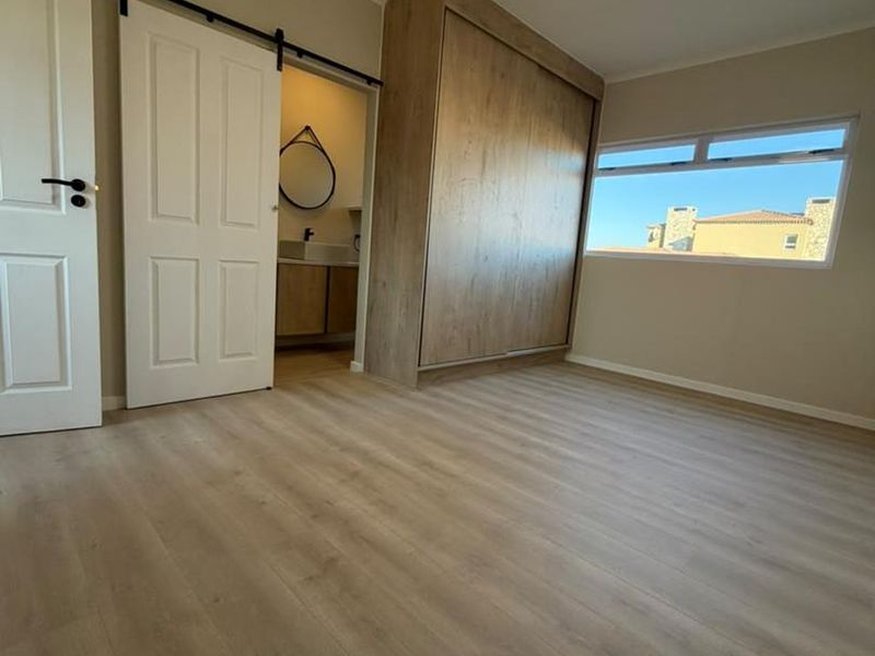 A bright, empty bedroom featuring modern laminate flooring, a large built-in wardrobe, and a sliding barn door leading to an en-suite bathroom.