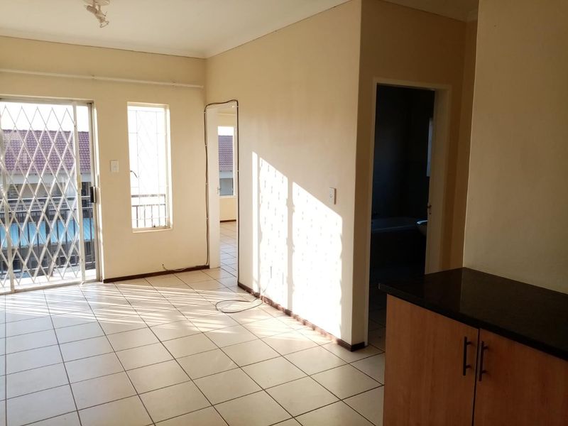 An open-plan living area featuring tiled flooring, a sliding door with security gate, and a kitchen corner with granite countertops.