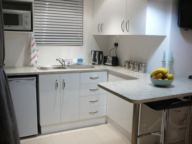 Compact modern kitchen featuring white cabinetry, granite countertops, a breakfast bar, and a built-in microwave.