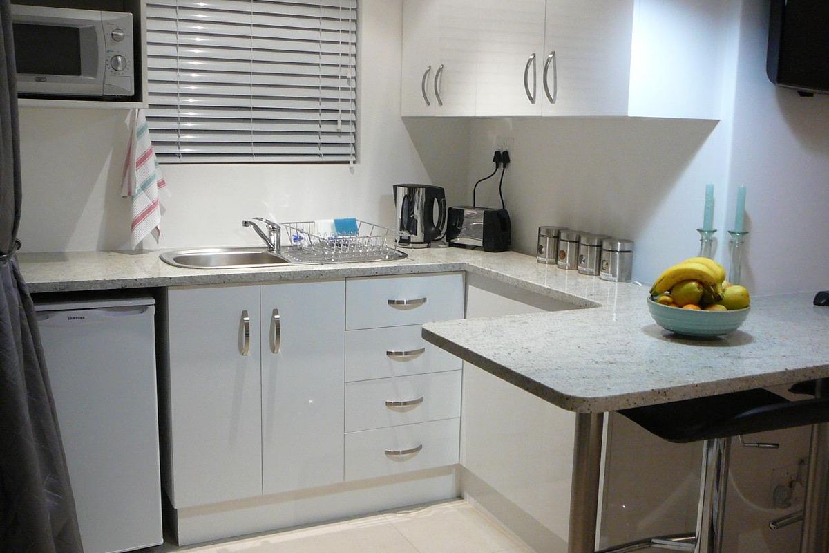 Compact modern kitchen featuring white cabinetry, granite countertops, a breakfast bar, and a built-in microwave.