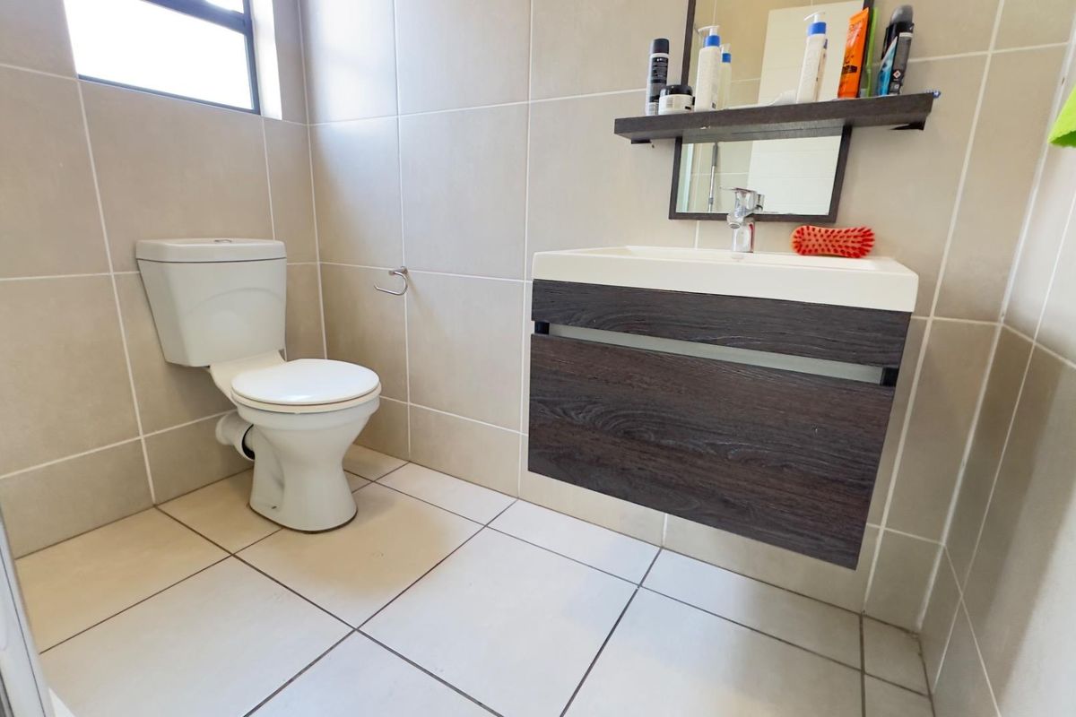 A modern bathroom featuring a wall-mounted vanity, ceramic toilet, and neutral floor-to-ceiling tiling.