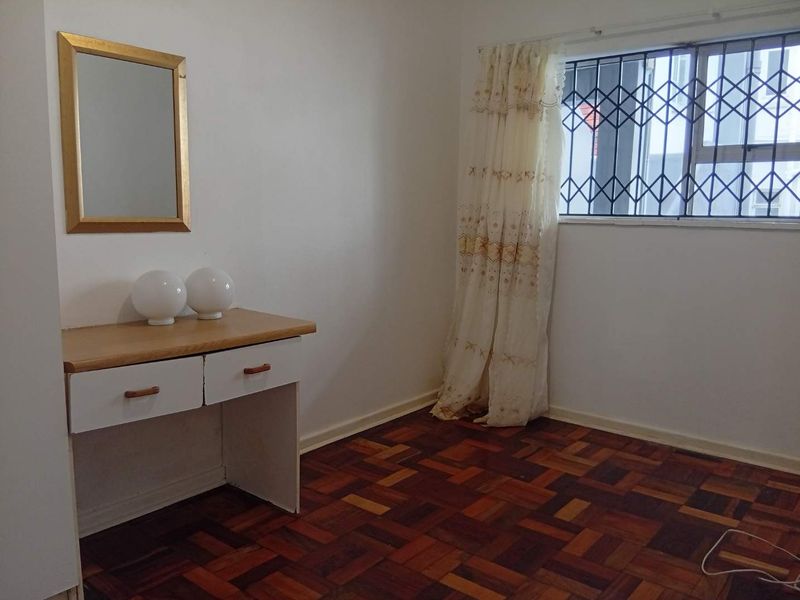 A bedroom featuring classic parquet flooring, a built-in vanity unit, and a window fitted with a security gate.