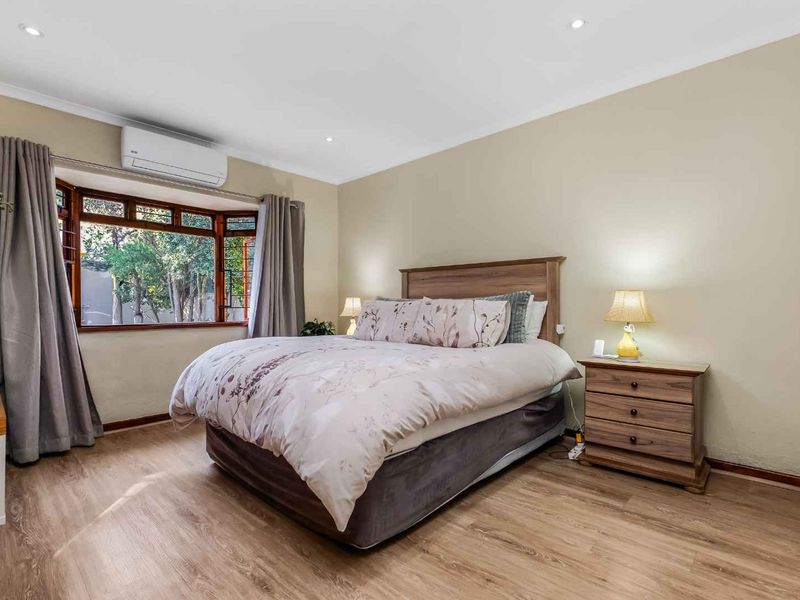 A well-maintained bedroom featuring laminate flooring, a bay window, and a wall-mounted split-system air conditioner.