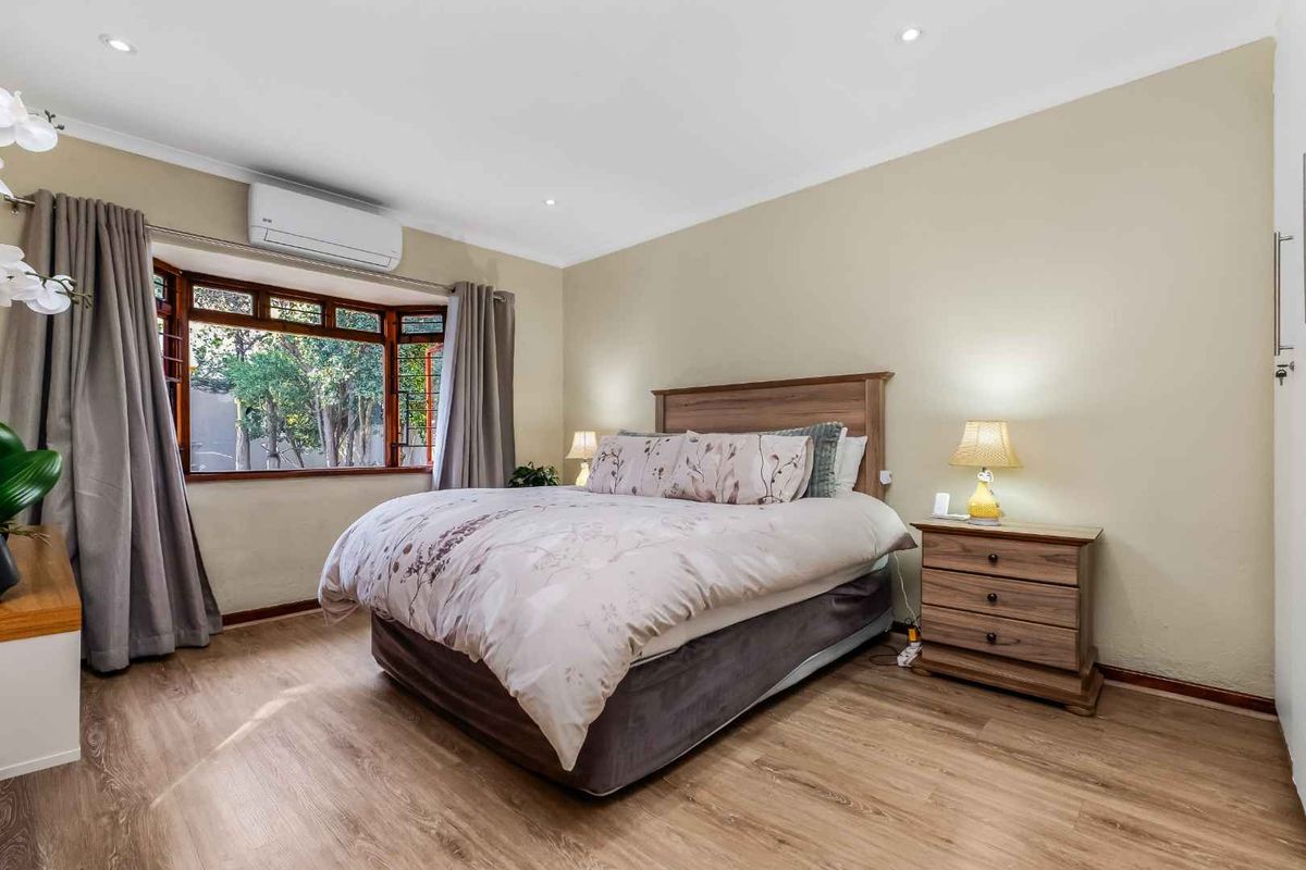 A well-maintained bedroom featuring laminate flooring, a bay window, and a wall-mounted split-system air conditioner.