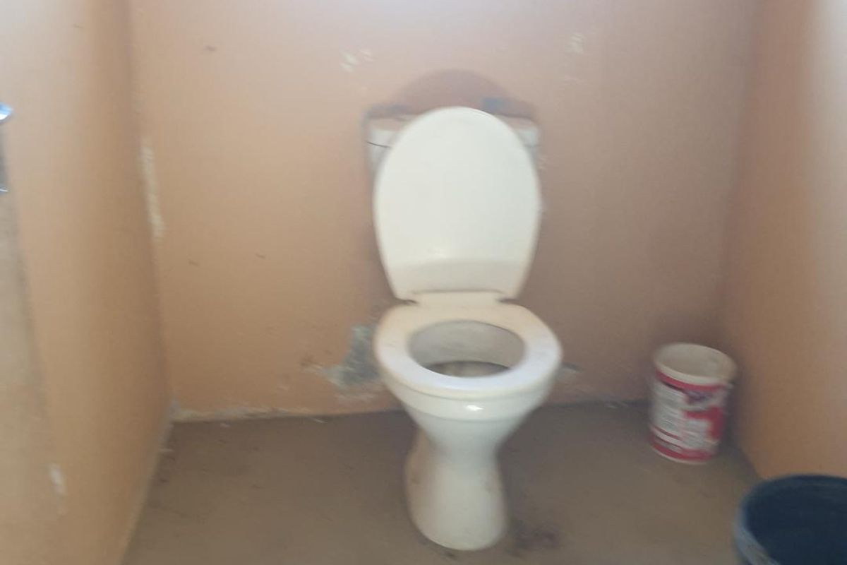 A basic industrial restroom facility featuring a standard toilet fixture with plain wall finishes and concrete flooring.
