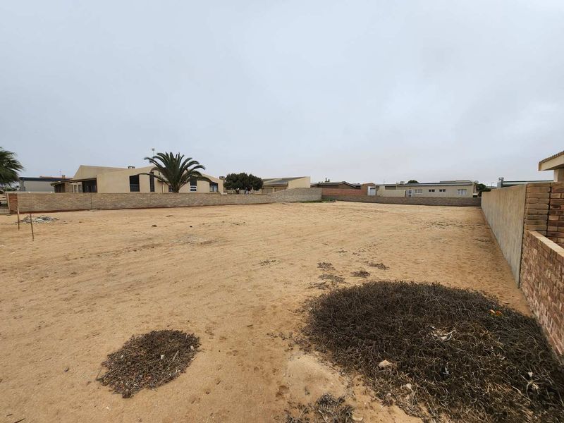 A vacant residential plot featuring sandy ground and enclosed by perimeter brick boundary walls in a developed neighbourhood.
