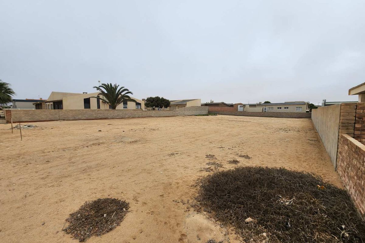 A vacant residential plot featuring sandy ground and enclosed by perimeter brick boundary walls in a developed neighbourhood.