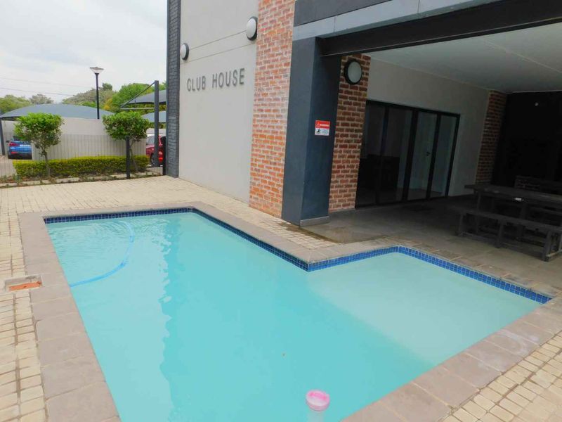 A well-maintained communal swimming pool area featuring a paved surround and an adjacent covered patio space at the clubhouse.