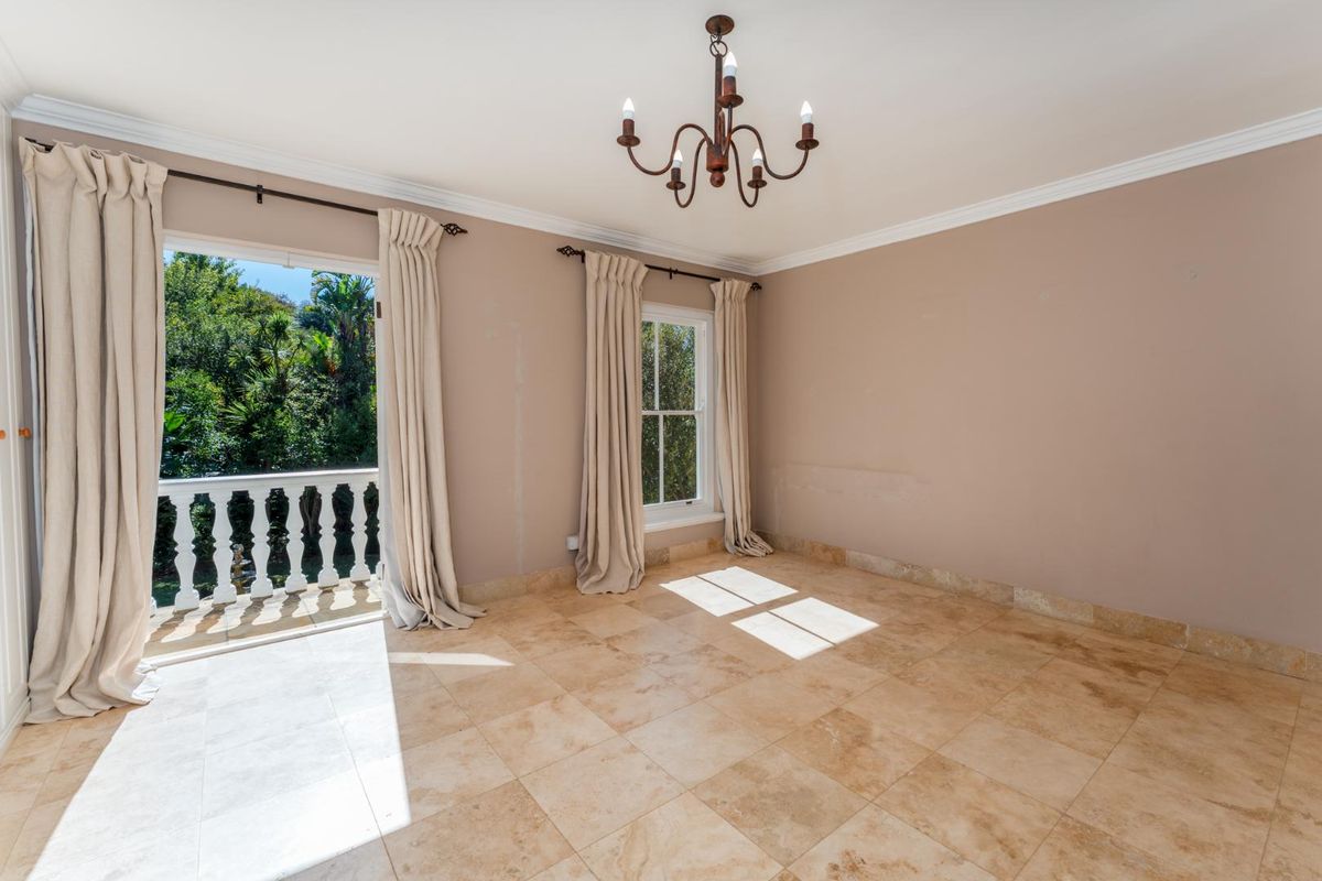 A spacious, empty bedroom featuring natural stone tile flooring, crown molding, a classic chandelier, and direct access to a private balcony.