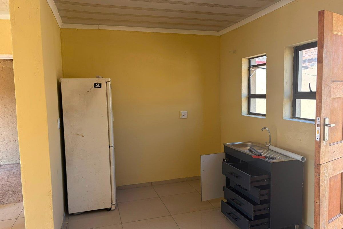 A compact kitchen area featuring tiled flooring, a stainless steel sink unit, and natural light from two windows.