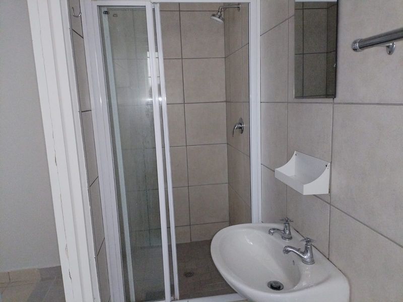 A functional bathroom featuring a tiled shower enclosure and a wall-mounted basin with dual-handle taps.