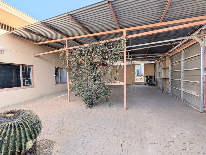 A spacious, covered outdoor garage area featuring paved flooring, a corrugated metal roof, and a steel support structure.