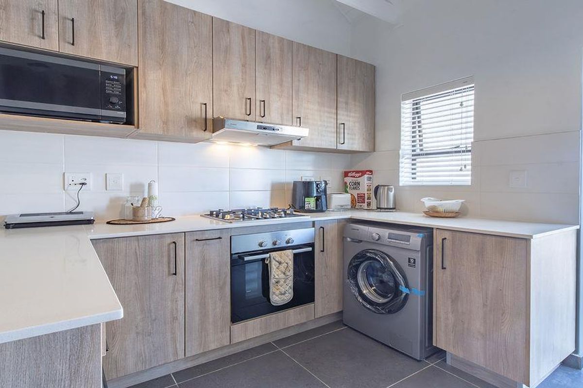 Modern kitchen featuring light wood-grain cabinetry, stone countertops, built-in gas hob, oven, extractor fan, and integrated laundry appliance space.