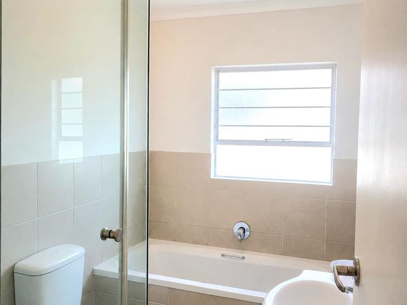 A clean, functional bathroom featuring a glass-enclosed shower, a built-in bathtub, a pedestal washbasin, and neutral tiled finishes.