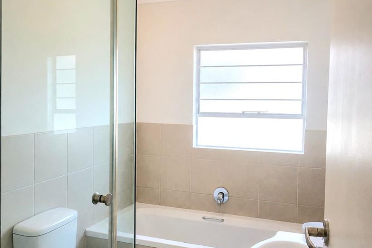 A clean, functional bathroom featuring a glass-enclosed shower, a built-in bathtub, a pedestal washbasin, and neutral tiled finishes.