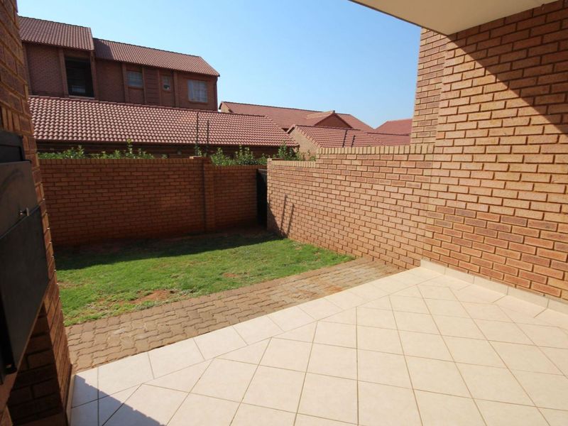A private covered patio featuring tiled flooring and a built-in braai, leading out to a small paved area and a compact garden.