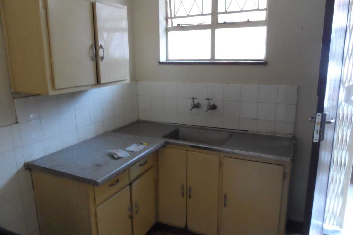 A dated kitchen area featuring original cabinetry, laminate countertops, a stainless steel sink, and tiled splashbacks, offering significant potential for modernization.