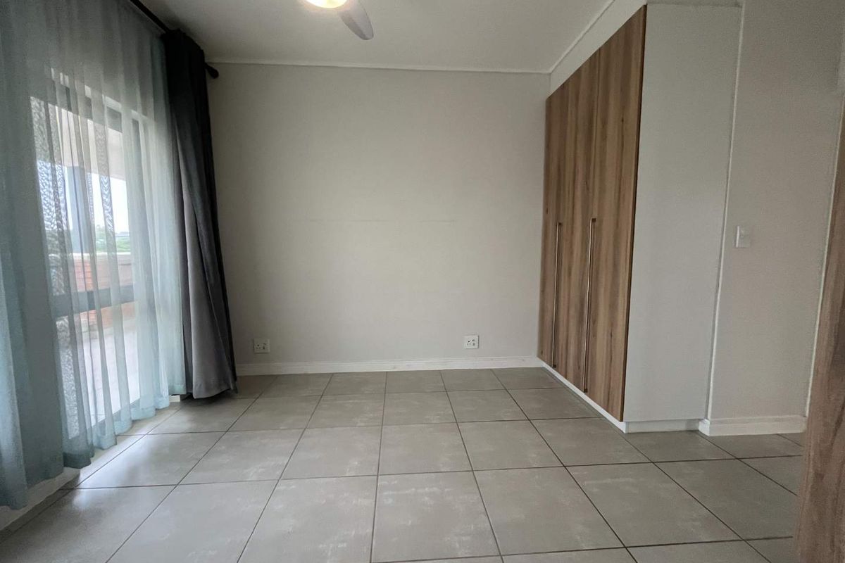 A bright, empty bedroom featuring modern tiled flooring, built-in wooden cupboards, and a sliding glass door leading to an outdoor area.