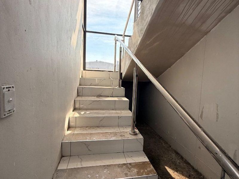Staircase area featuring tiled steps, a stainless steel handrail, and a large window, currently in an unfinished state requiring completion and cleaning.