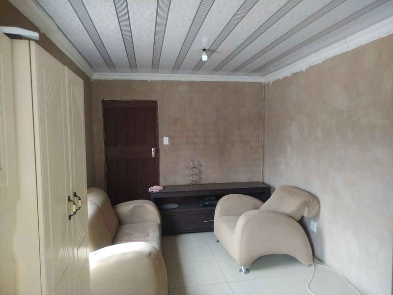 A living room space featuring tiled flooring and a panelled ceiling, currently requiring wall finishing and cosmetic updates to improve the overall aesthetic.