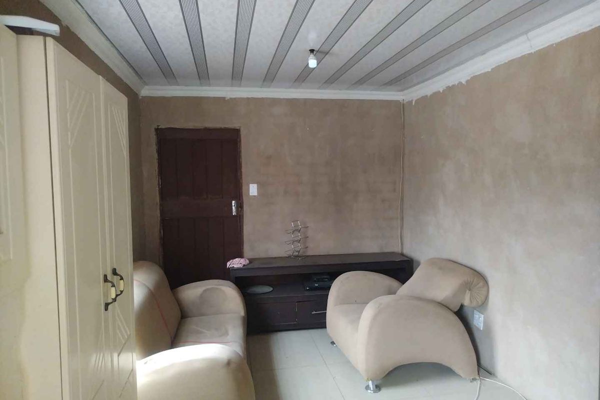 A living room space featuring tiled flooring and a panelled ceiling, currently requiring wall finishing and cosmetic updates to improve the overall aesthetic.