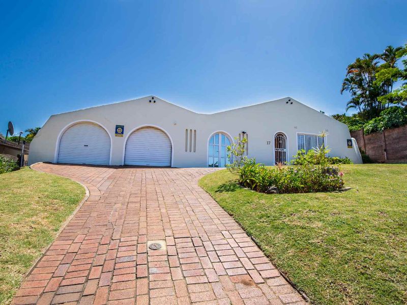 Front elevation of a single-story house featuring a paved driveway, double garage with arched doors, and a landscaped front garden.