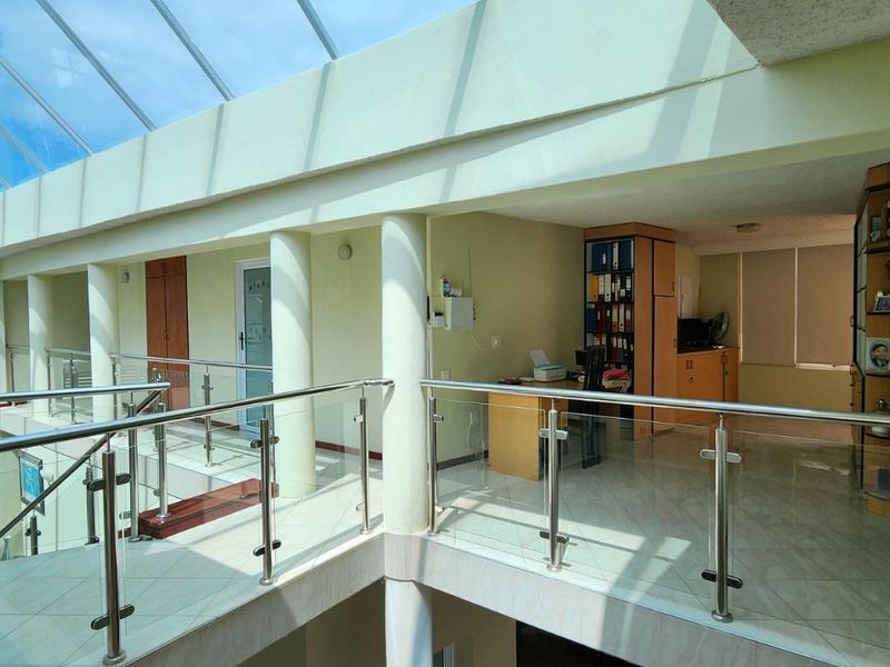 Spacious upper-level landing featuring a large glass skylight, modern stainless steel and glass balustrades, and tiled flooring.
