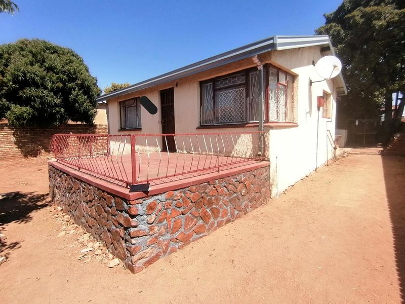 Rear view of the house featuring a raised stone-clad patio with metal security railings and security bars on the windows.