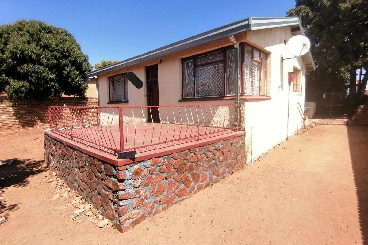 Rear view of the house featuring a raised stone-clad patio with metal security railings and security bars on the windows.