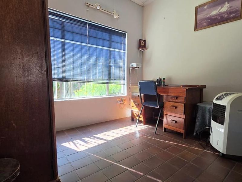 A functional bedroom featuring tiled flooring and natural light through a window fitted with venetian blinds.