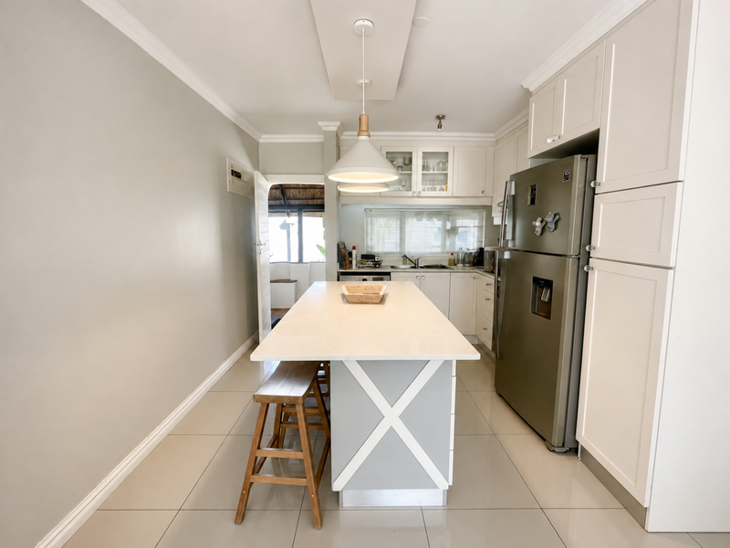 Modern kitchen featuring a central island with quartz countertops, shaker-style cabinetry, pendant lighting, and tiled flooring, offering a clean and functional workspace.