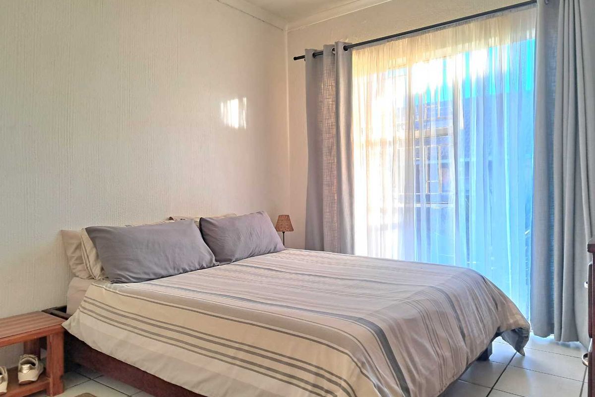 A bedroom featuring tiled flooring and a large window with curtains, providing natural light and access to the exterior.