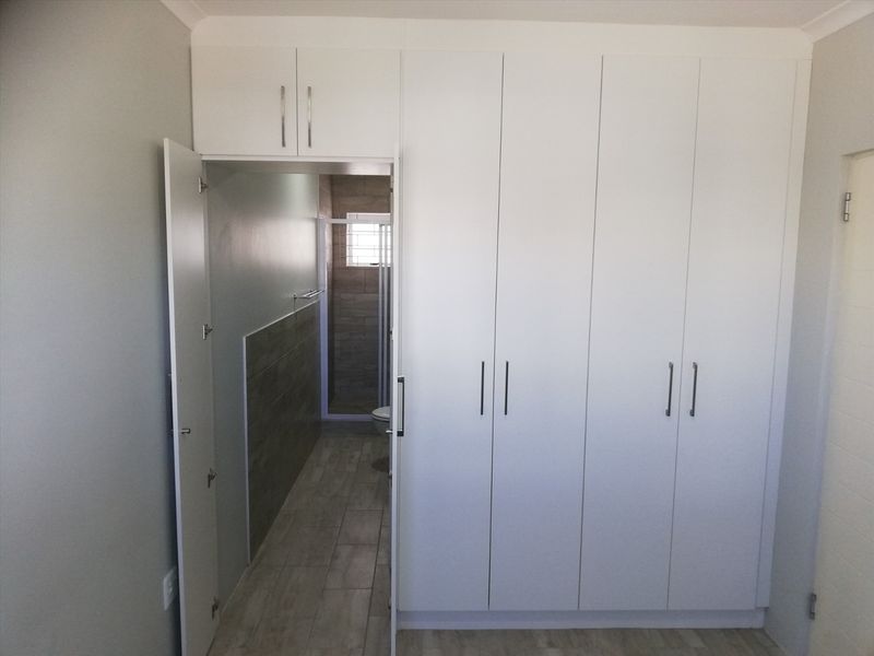 A clean bedroom featuring modern white built-in cupboards and direct access to an en-suite bathroom with tiled finishes.