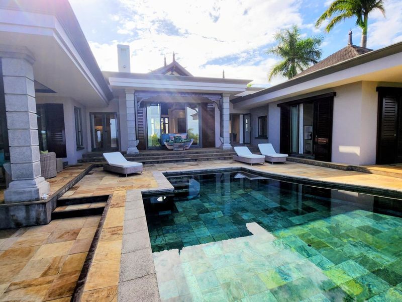 A luxurious outdoor pool area featuring a stone-tiled deck, covered patio spaces, and elegant stone columns, perfect for relaxation and outdoor entertaining.